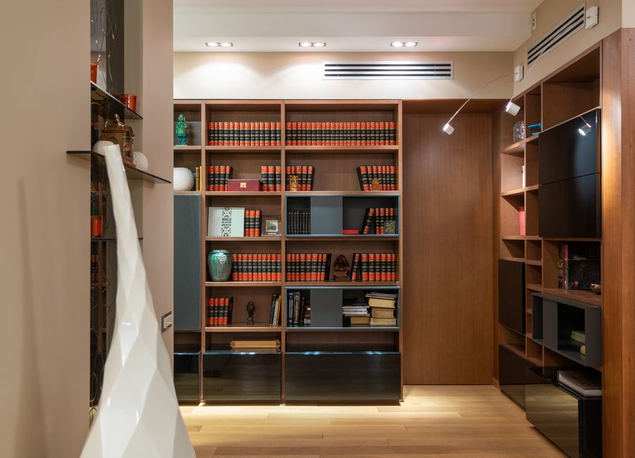 Rows of books placed on wooden bookshelves in spacious room in modern apartment